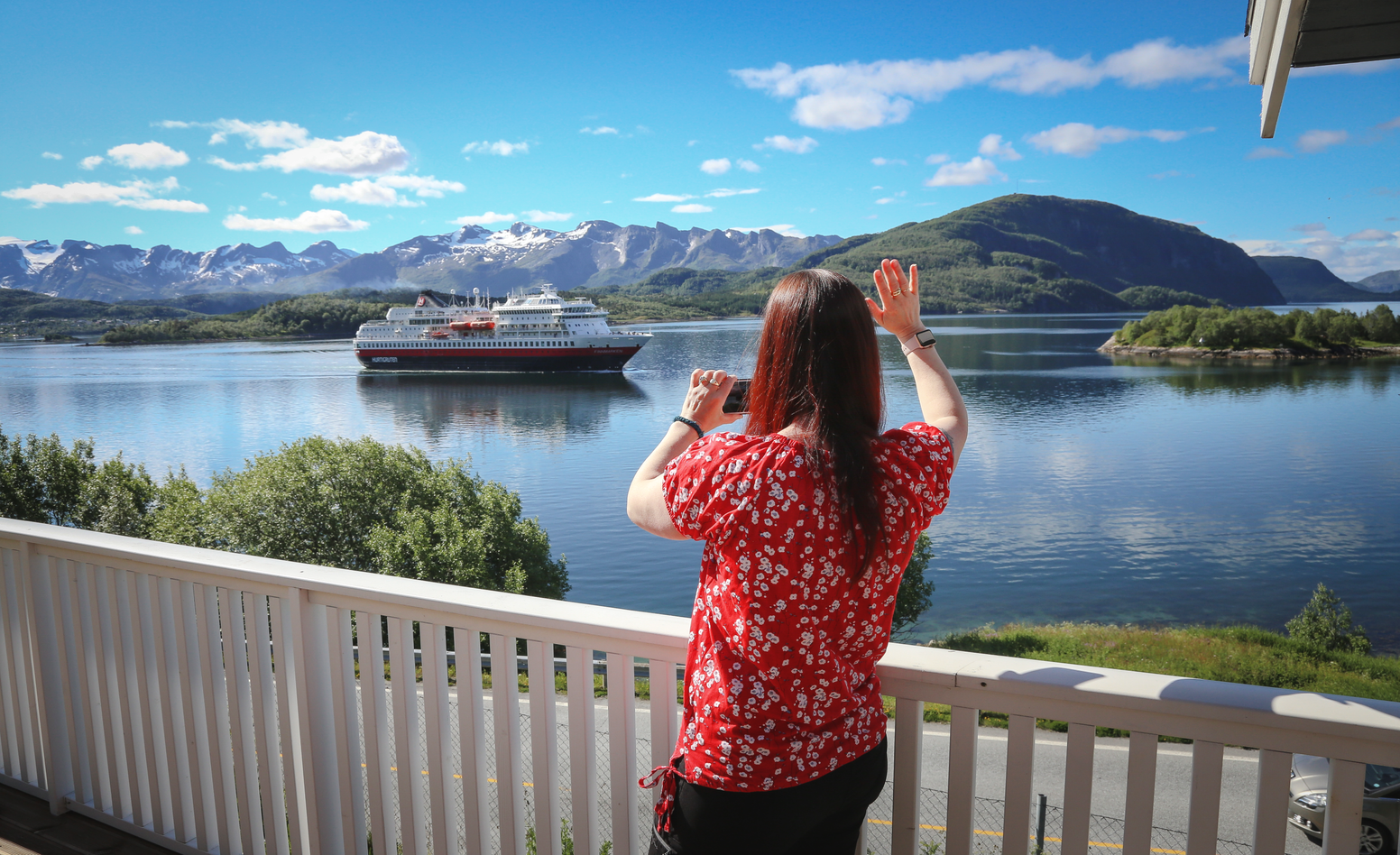 Eva Randel vid sitt hus och vinkar till Hurtigruten som passerar